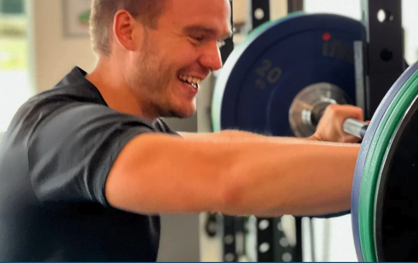 A man lifting weights at a gym, smiling and focused on his exercise.