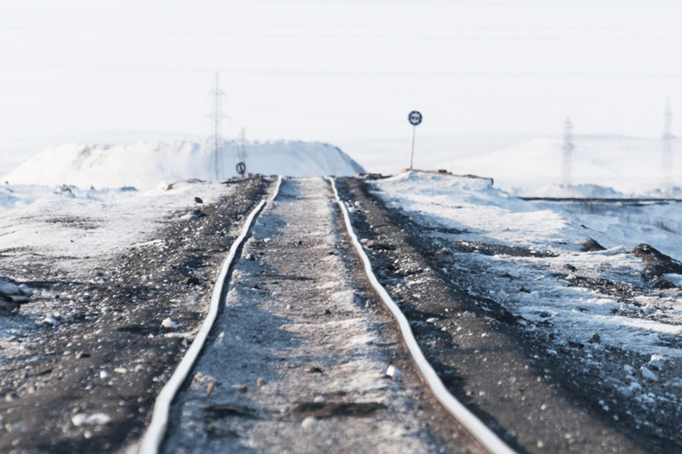 Snow-covered railroad tracks extending into the horizon with power lines and a snow-covered landscape in the background.