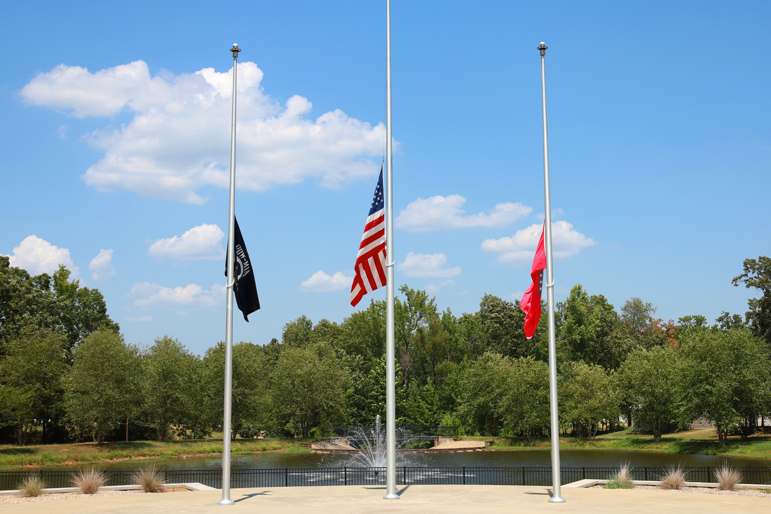 Three flagpoles displaying the POW/MIA flag, American flag, and Arkansas state flag in front of Arkansas State Veterans Cemetery at North Little Rock.