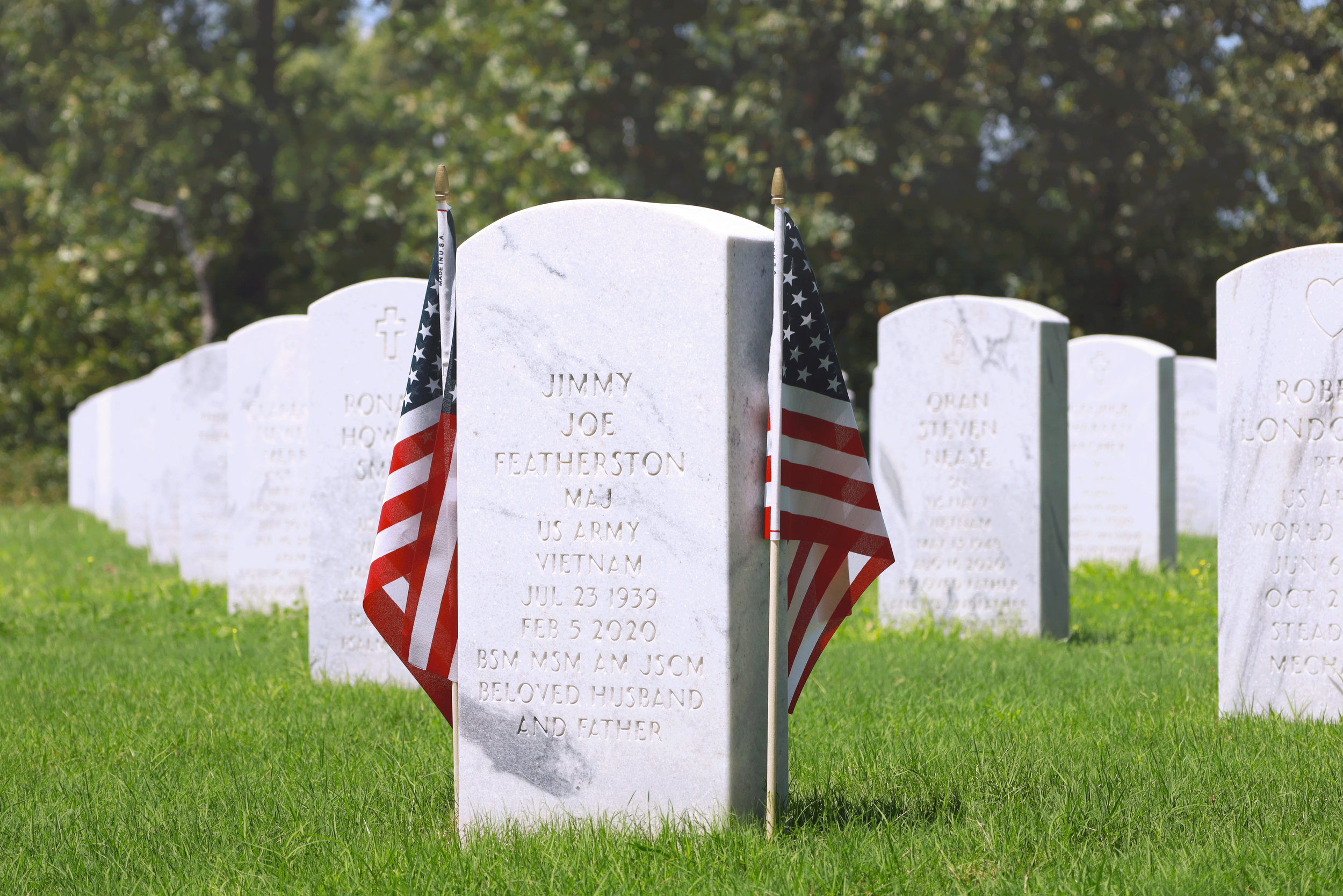 Grave site with a white headstone adorned with American flags at Arkansas State Veterans Cemetery in North Little Rock.