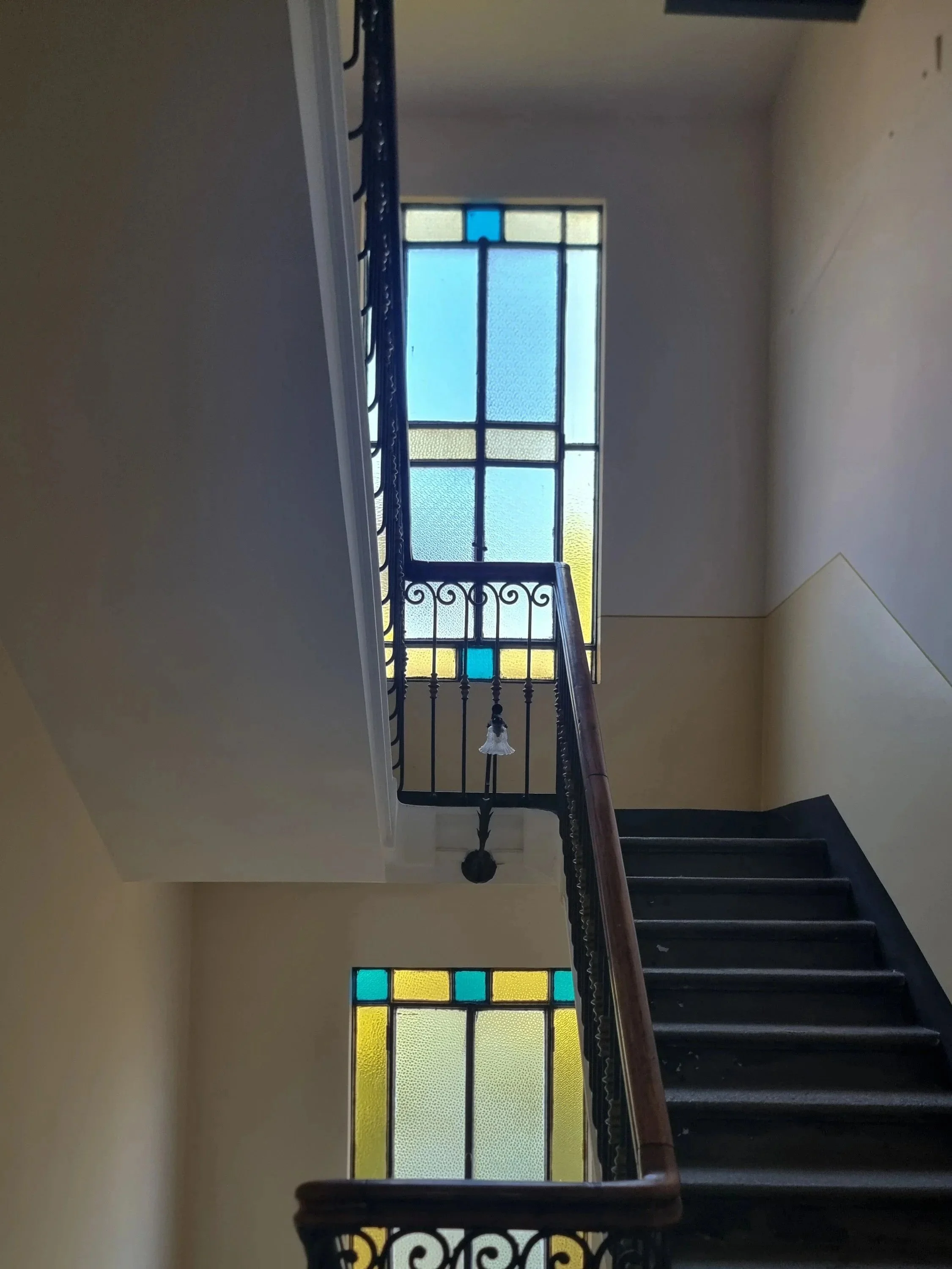 Vista di una scala con ringhiera in ferro battuto e vetri colorati alla finestra superiore, in un edificio residenziale.