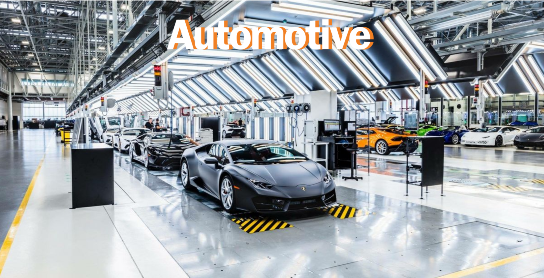 Interno di una fabbrica di automobili con molte auto sportive di lusso, tra cui Lamborghini, in fase di produzione, con impianti e attrezzature industriali intorno.