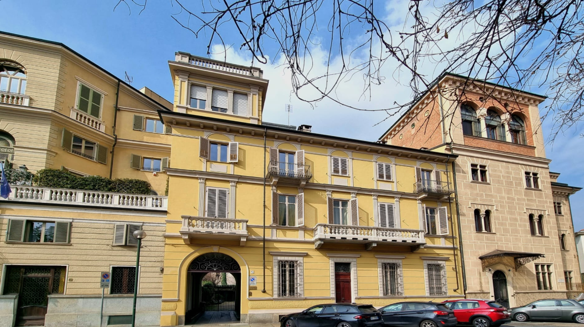 Edificio residenziale di tre piani con balconi e finestre, color giallo e beige, con alcuni piani più alti e un cielo blu sopra
