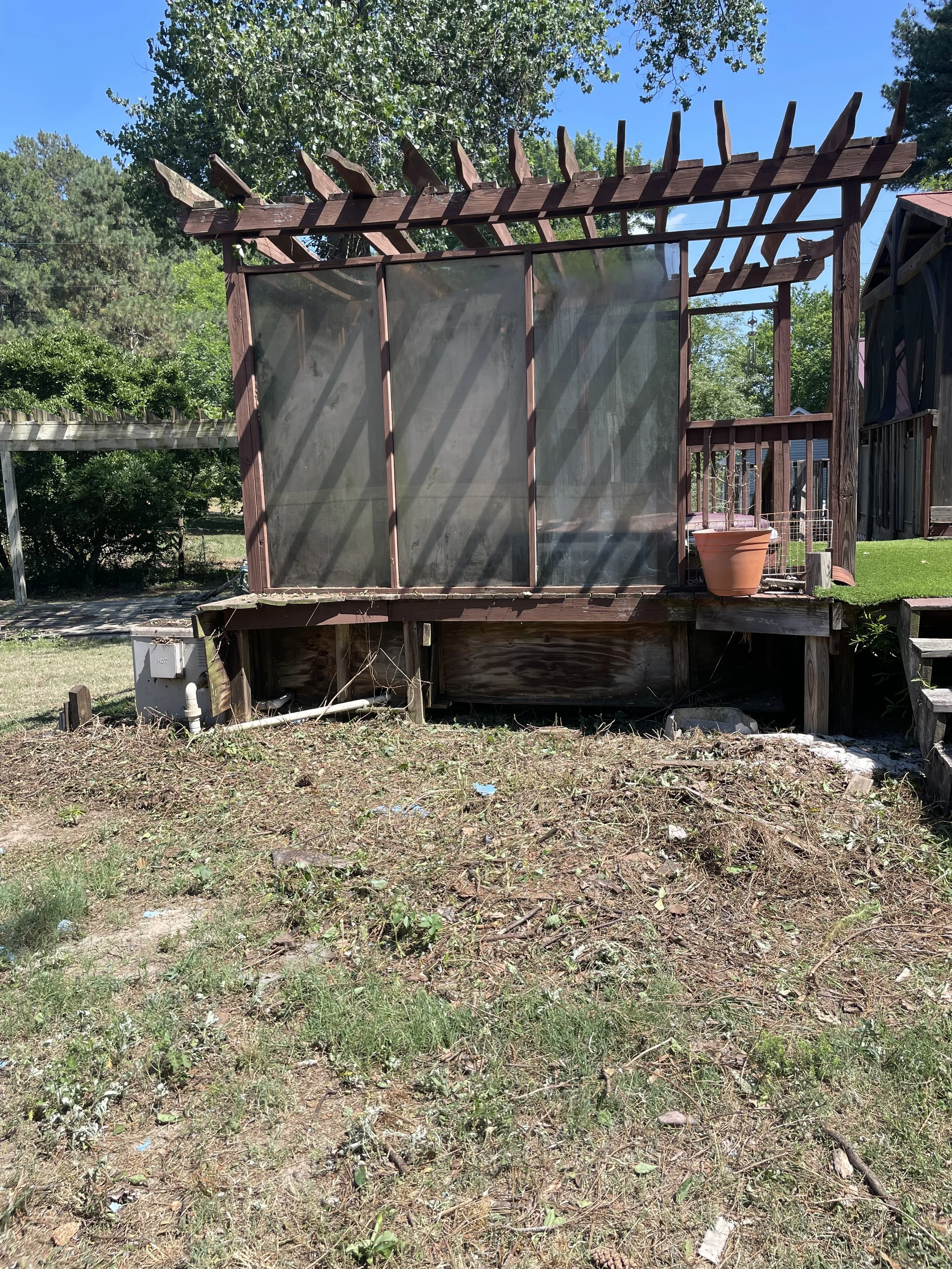 A backyard with a wooden gazebo or patio cover under a blue sky, freshly cleaned from brush & other yard debri removal.