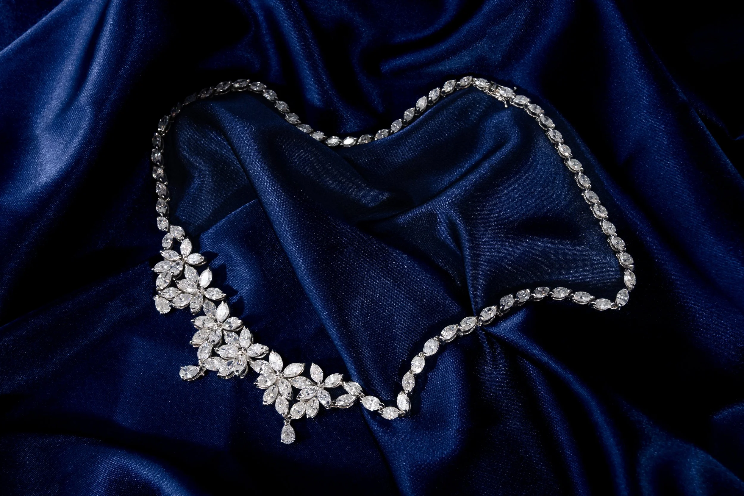 A diamond necklace and matching earrings resting on dark blue satin fabric.