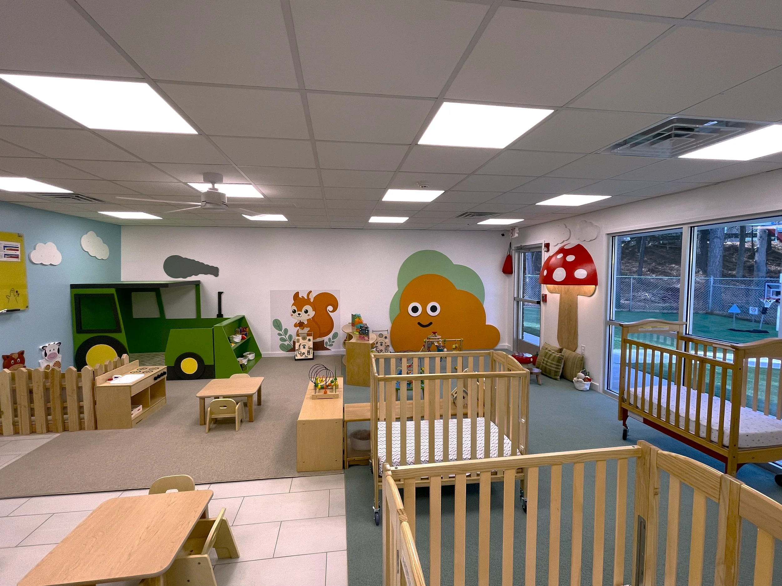 Colorful preschool or daycare room with wooden furniture, animal wall decals, and large windows letting in natural light.