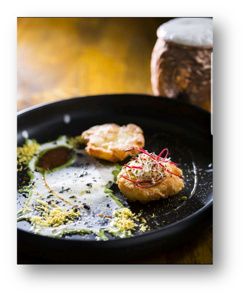 Fried food on a black plate with garnishes, next to a container of salt.
