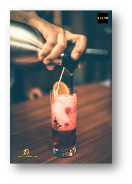 A bartender pouring a pink cocktail with bubbles into a glass, garnished with an orange slice, at a bar counter.
