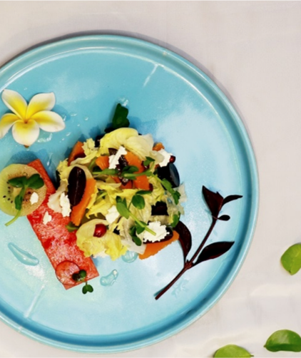 A colorful salad with various vegetables and toppings on a light blue plate decorated with a yellow flower and dark leaves.