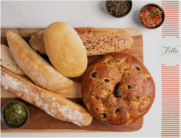 Assorted breads and two small bowls of dipping sauces on a wooden cutting board.