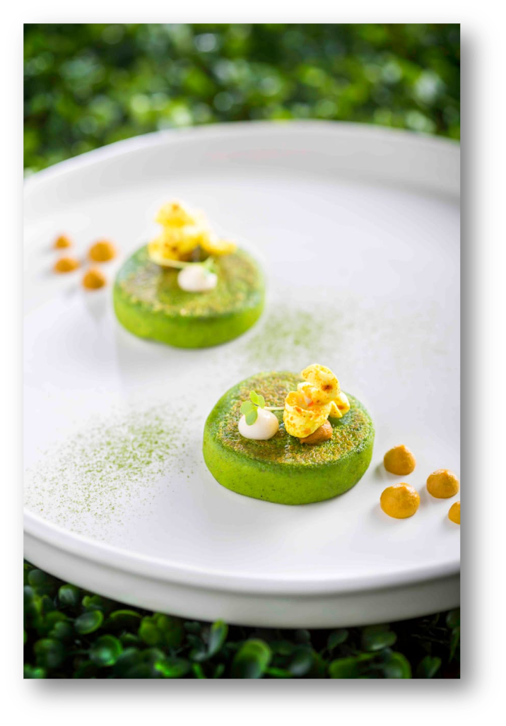 Two green vegetable dishes garnished with yellow and white toppings, served on a white plate with a green background.