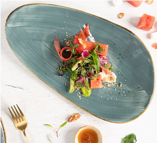 A gourmet appetizer of smoked salmon, fresh greens, and edible flowers on a blue oval plate.