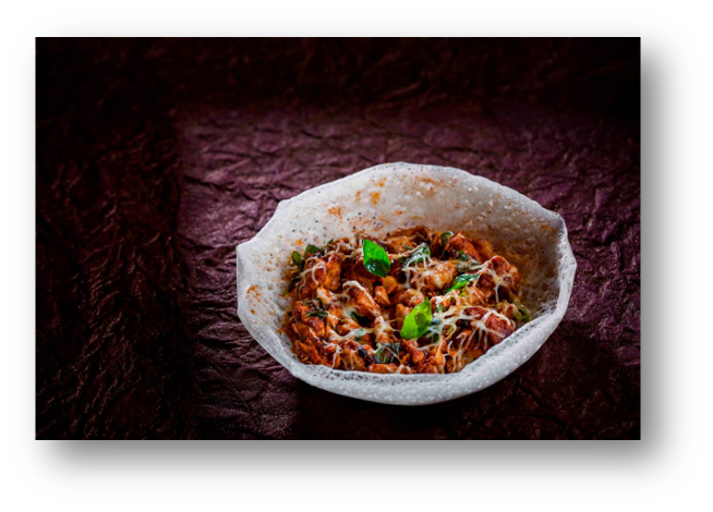 A bowl of spicy chili garnished with green herbs, served on a dark textured surface.