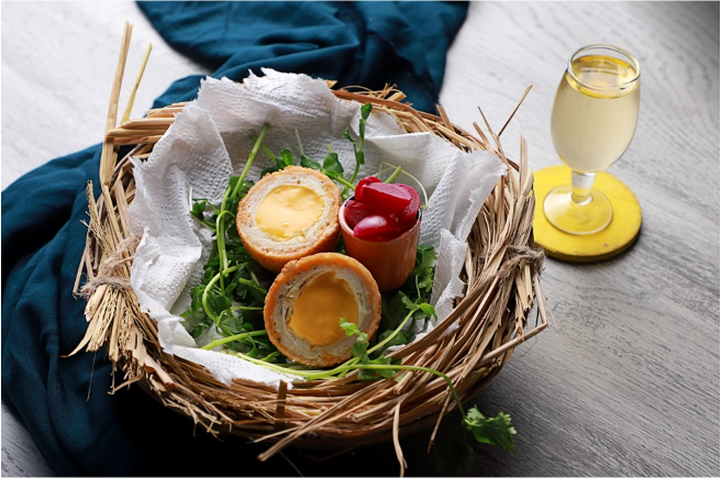 Basket with deep-fried cheese-stuffed eggs, some leafy greens, and a small container of red cherries, with a glass of white wine nearby.