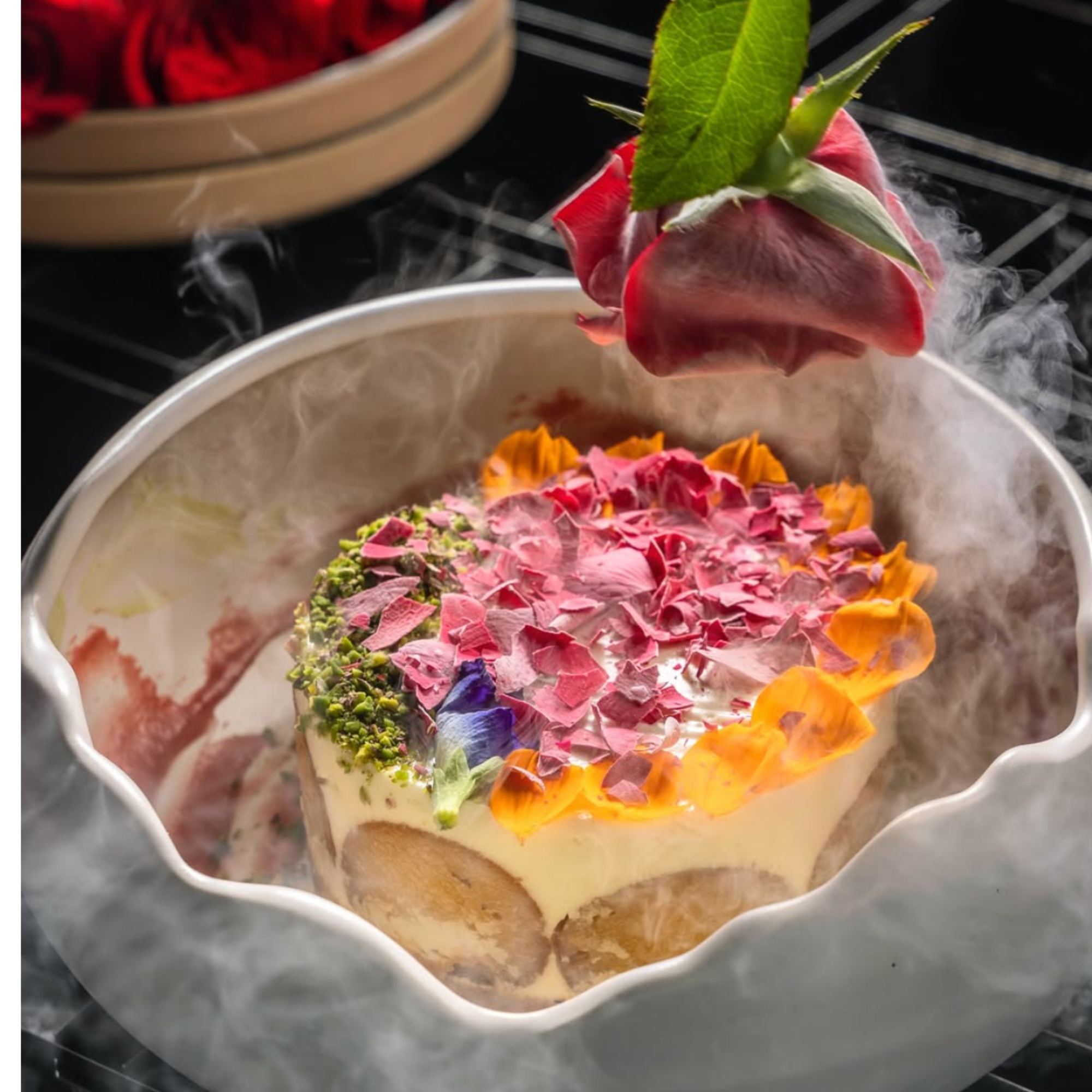 A steaming bowl of colorful edible flower petals, with a green leaf on top, placed on a marble surface.