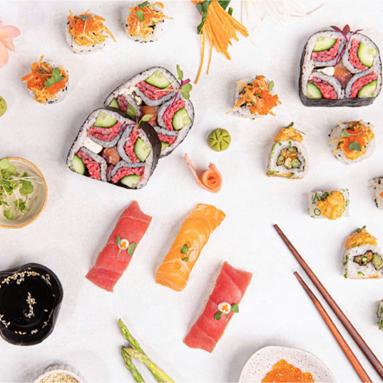 Assorted sushi rolls, sashimi, and garnishes on a white surface.