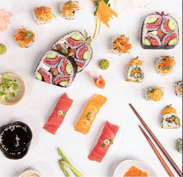 Assorted sushi rolls, including salmon and tuna nigiri, arranged on a white surface with chopsticks, soy sauce, and garnishes.