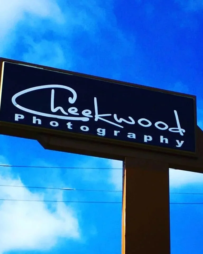 Sign for Cheekwood Photography against a blue sky with clouds, mounted on a tall post.