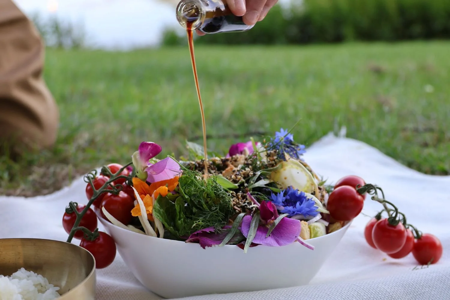 Close up of a colourful salad being dressed on a white blanket in a park setting for a gourmet picnic — Kilted Chicken by Chef Rodney Wages