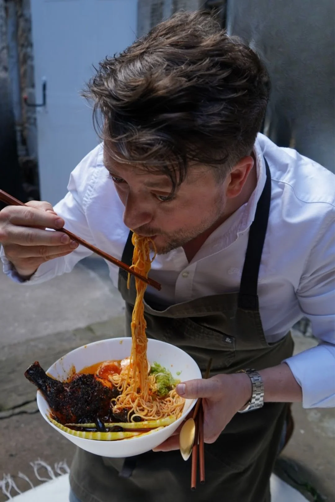 Chef Rodney Wages using chopsticks to eat from a bowl of chicken street food he's made in the kitchen — Kilted Chicken