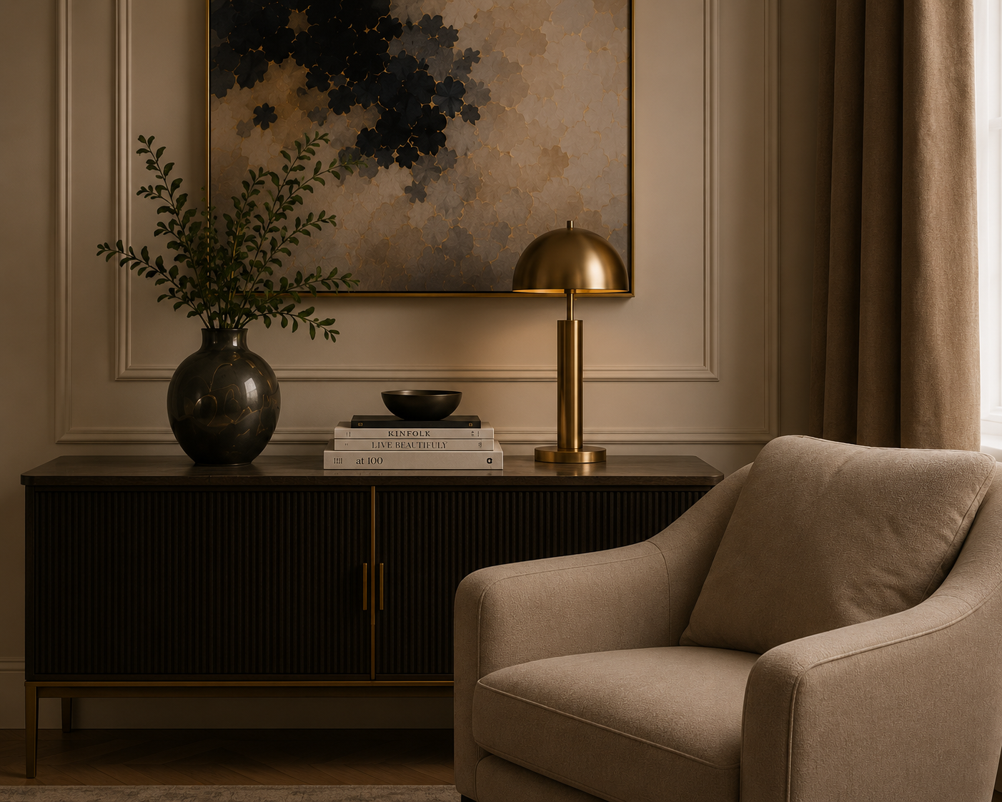 Living room sideboard decorated with a black vase and green leafy branch, a gold desk lamp, and a stack of art books, with wall art and beige curtains behind.