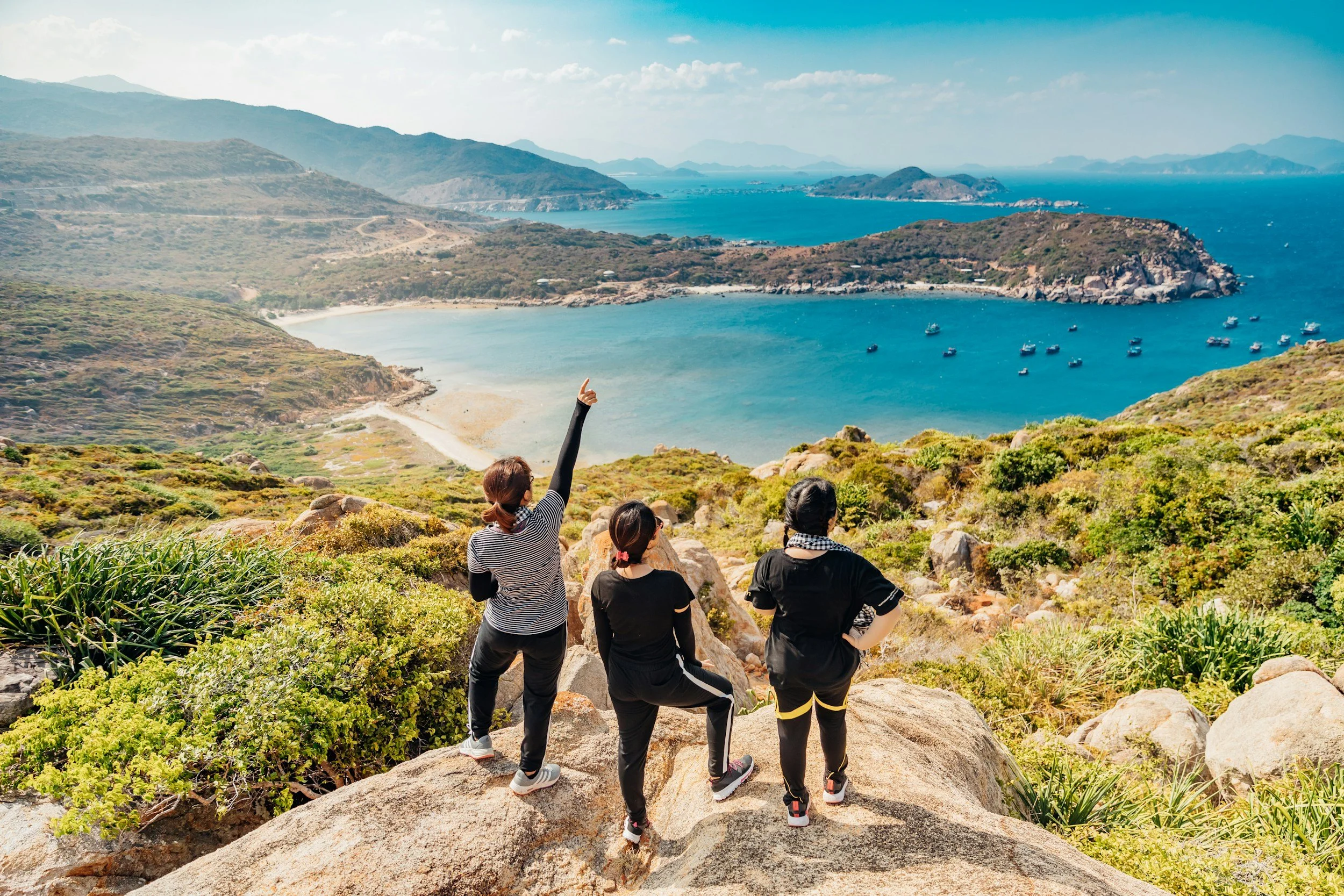 Three friends at the end of a hike overlooking a beautiful, blue ocean bay