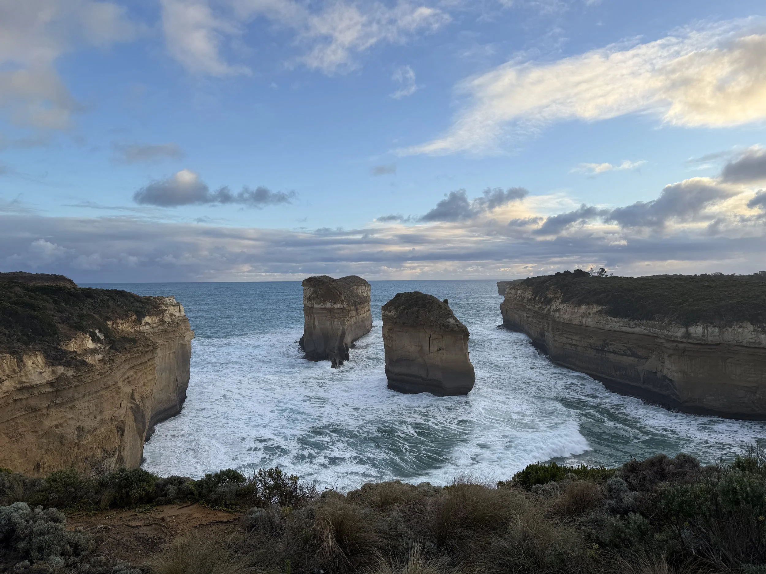 Cliffs and rock formations along a coastline with a cloudy sky and ocean waves below.