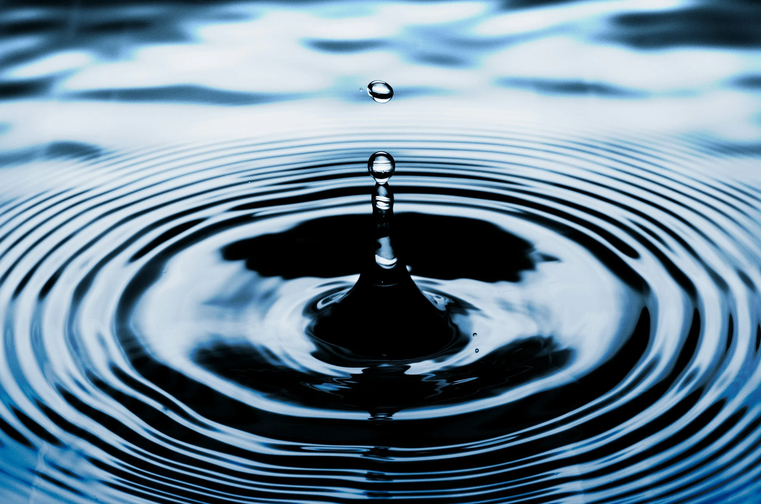 Close-up of a water droplet creating ripples in a calm water surface.