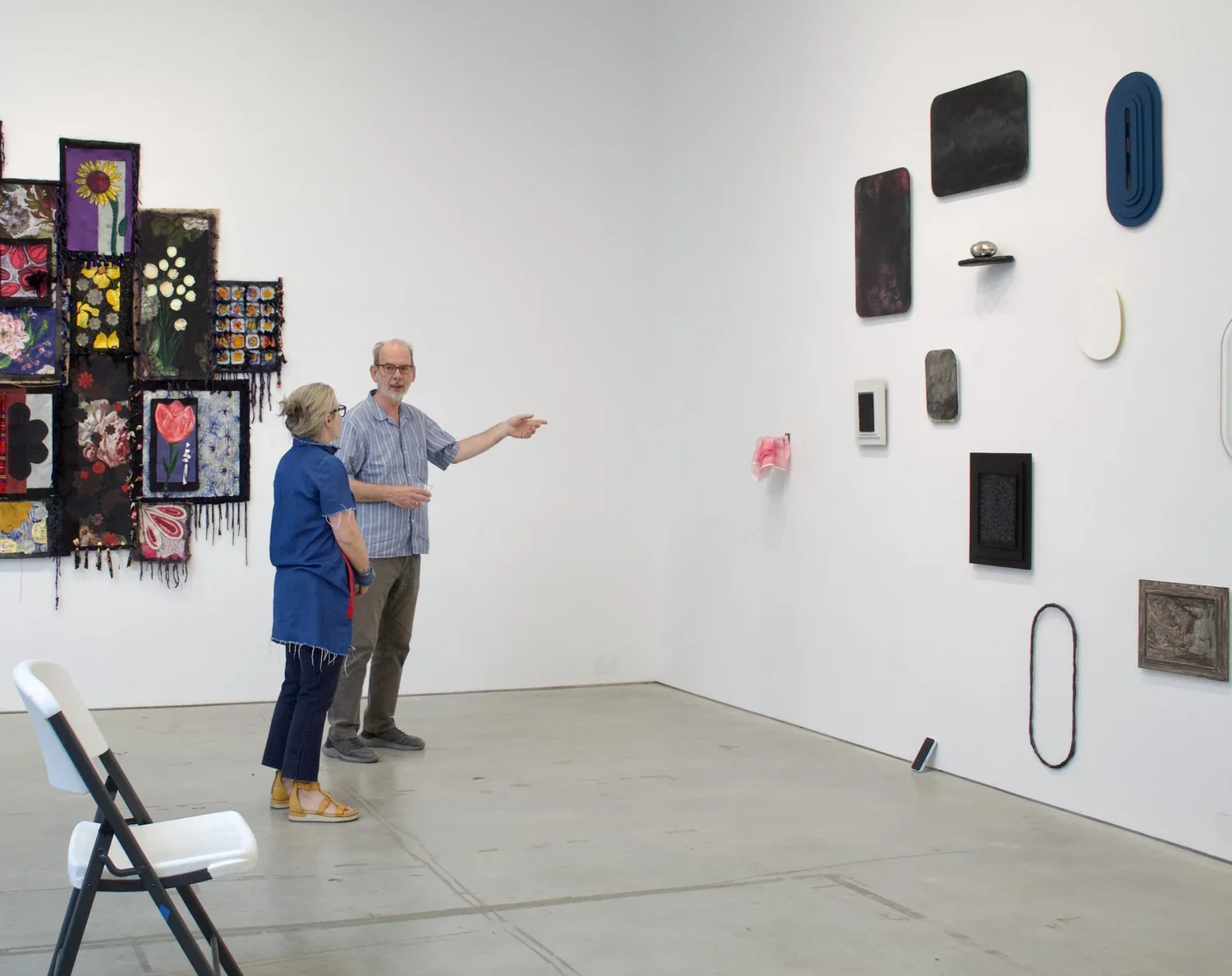Two people talking in an art gallery, with various abstract and textile art pieces on the walls.