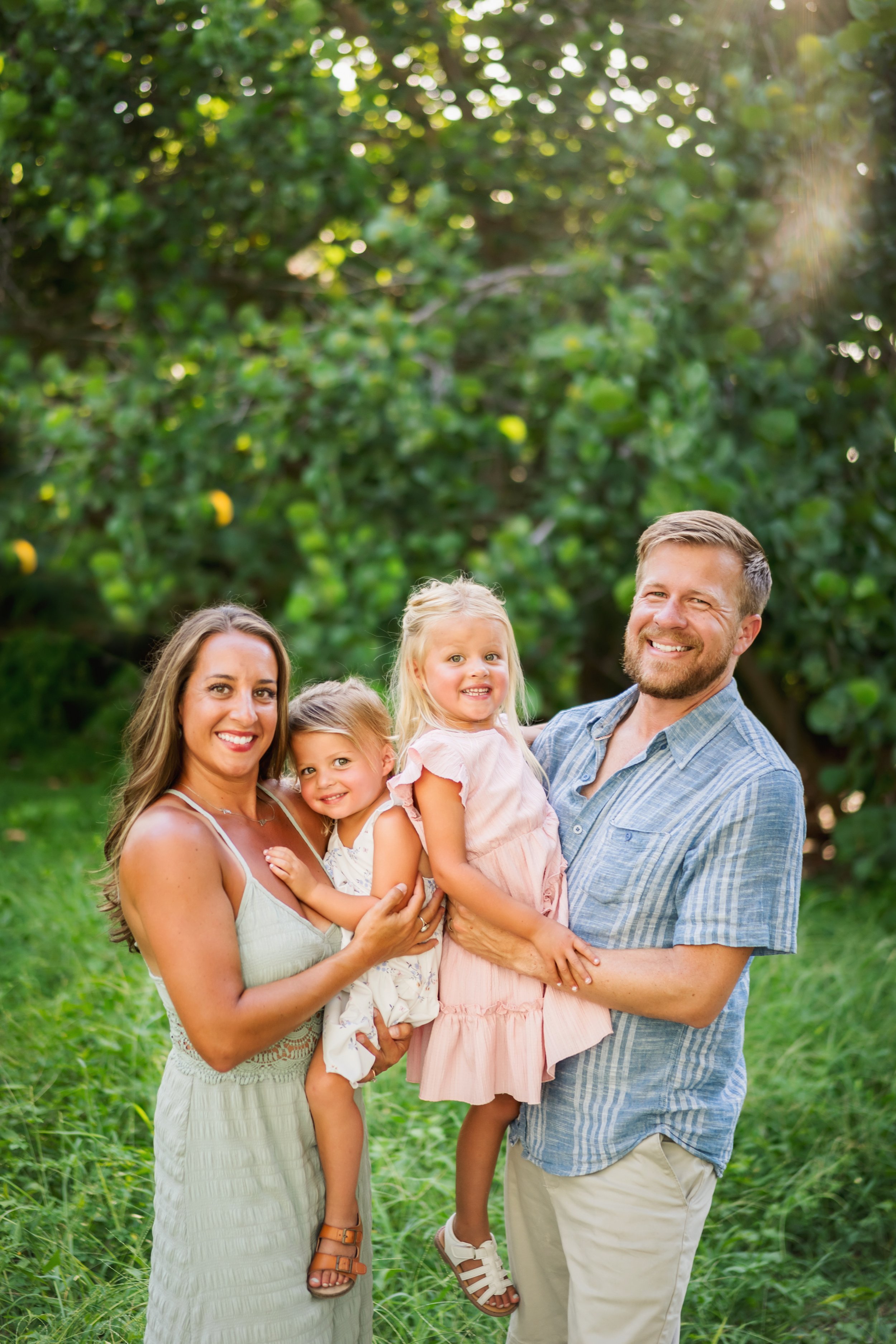 A happy family of five standing outdoors in a lush green park, smiling and embracing each other on a sunny day.