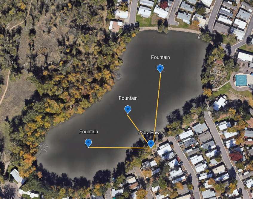 Aerial view of a pond with three fountains and a central connection labeled '230V Power,' surrounded by trees and residential houses, with a backyard pool visible in the upper right corner.