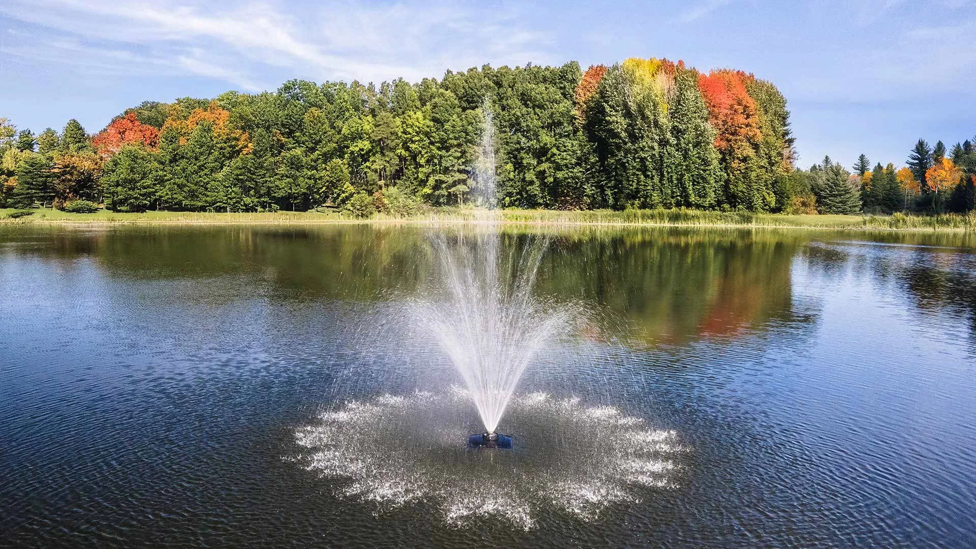 Pond aerating fountain spray surrounded by trees, installed by Still Waters Pond Management