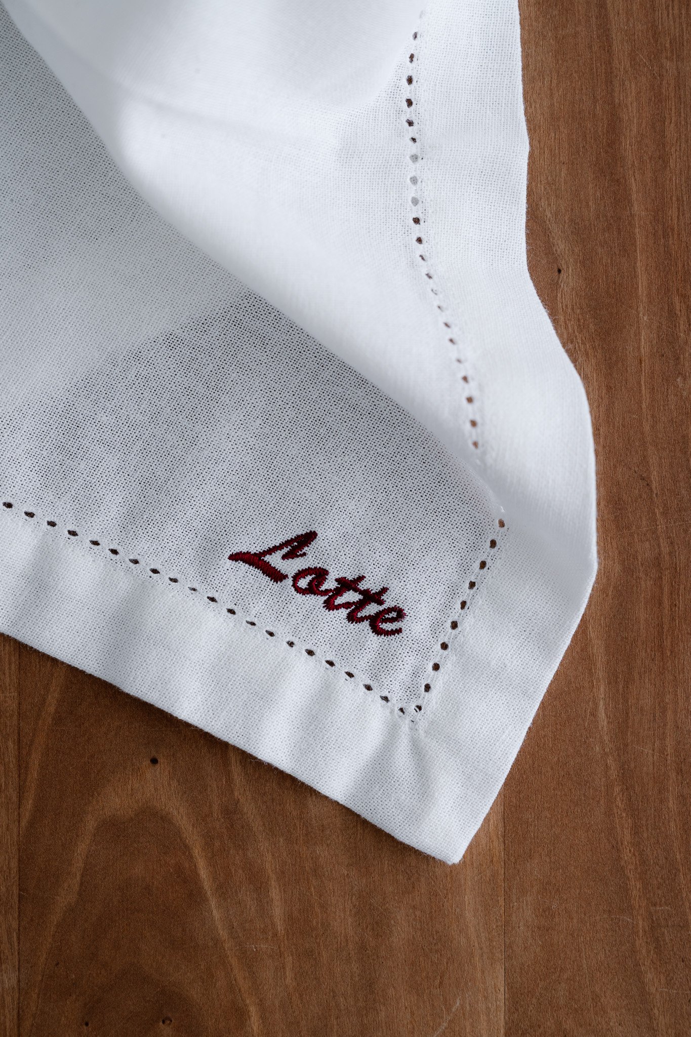 A close-up of a white fabric with embroidered red text reading 'Lattice' on a wooden surface.