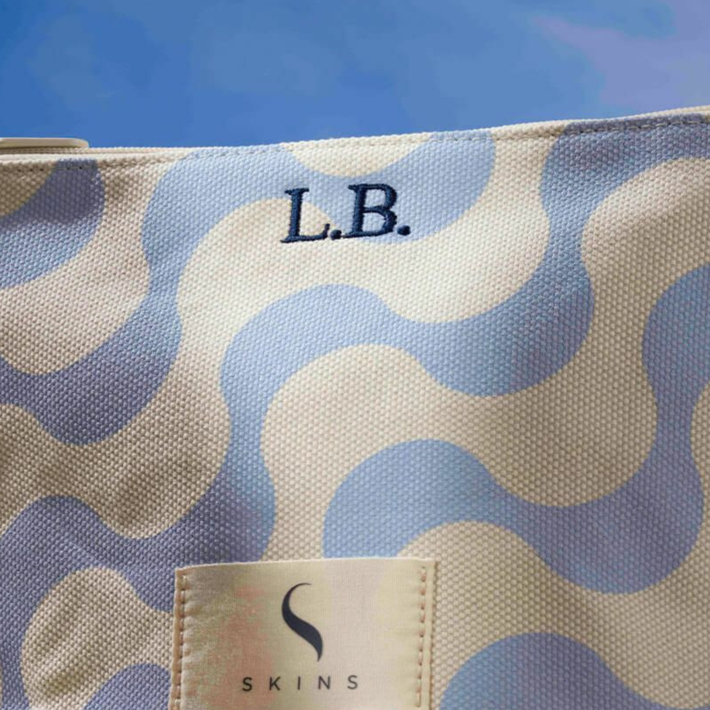 Close-up of a fabric label with the brand name 'Skins' and the size 'S' on a patterned background with blue and beige circles.