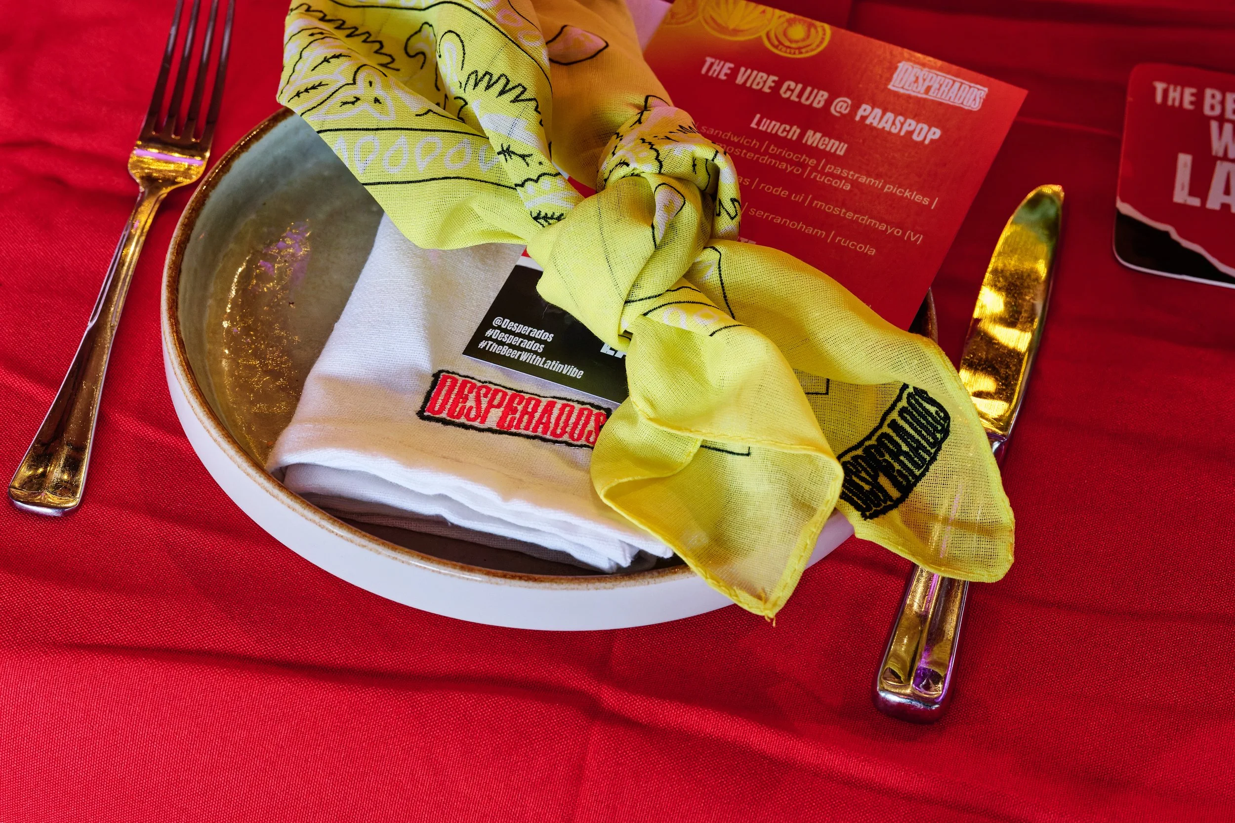 Place setting with gold utensils, a yellow napkin, and a divided plate on a red tablecloth, with a red placemat and menu in the background.