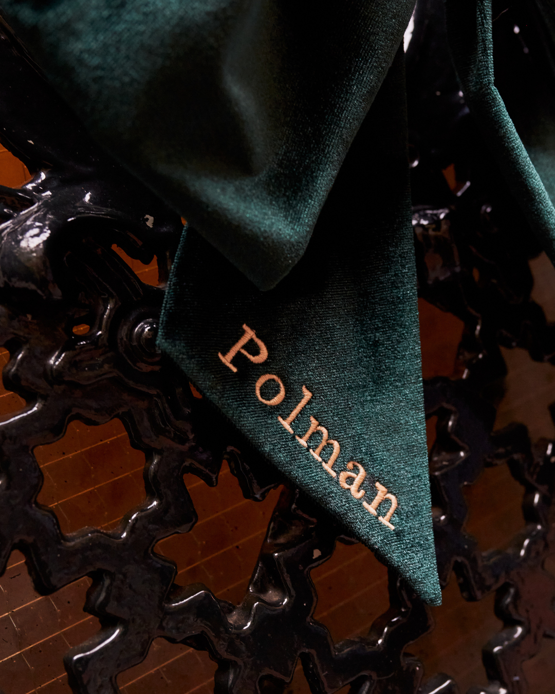 Close-up of a black bicycle chain with a green fabric cloth draped over it, with the word 'Polman' embroidered on the cloth.