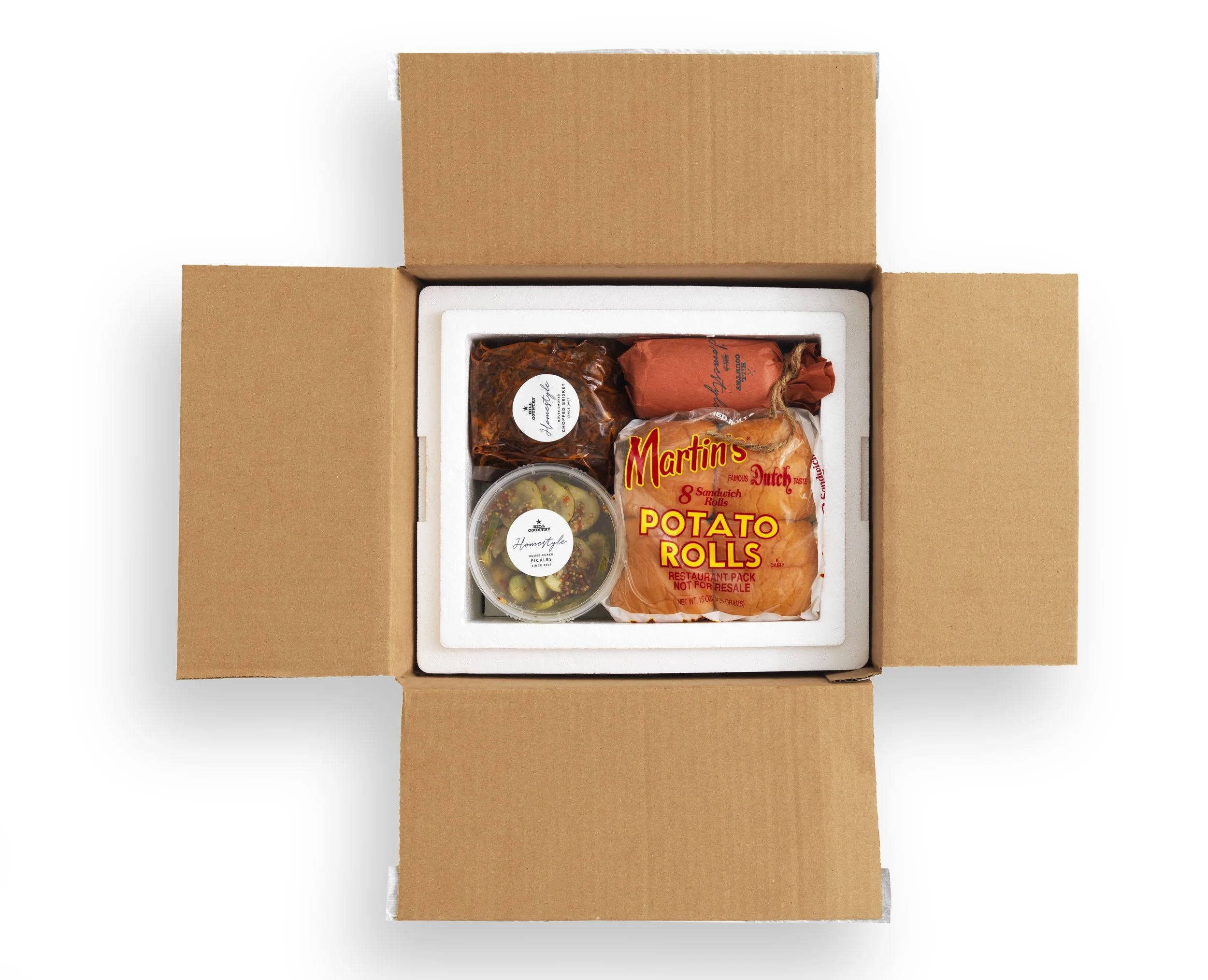 Hill Country Homestyle barbecue kit packed in an open insulated shipping box with rolls, meat and sides.