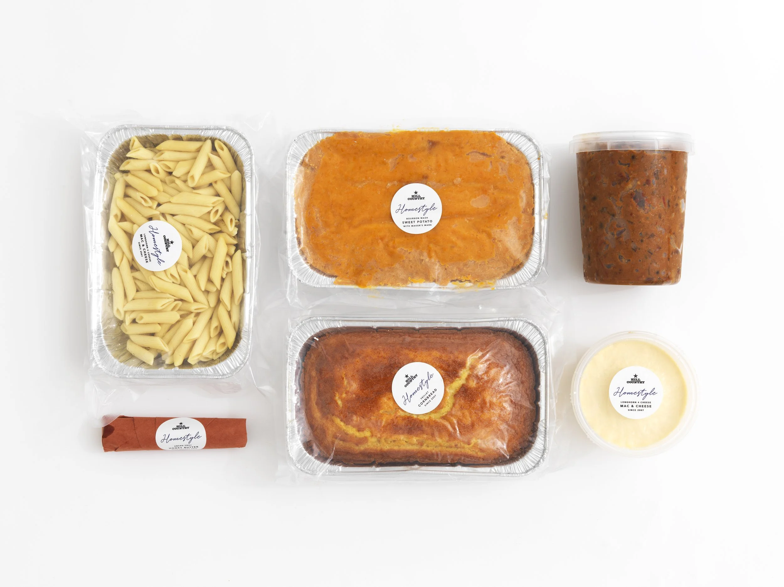 Hill Country Homestyle side-dish kit with prepared trays, a wrapped item and labeled tubs arranged on white.