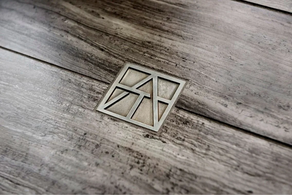 Artistic Tile metallic monogram set into dark, wood-grain patterned tile.