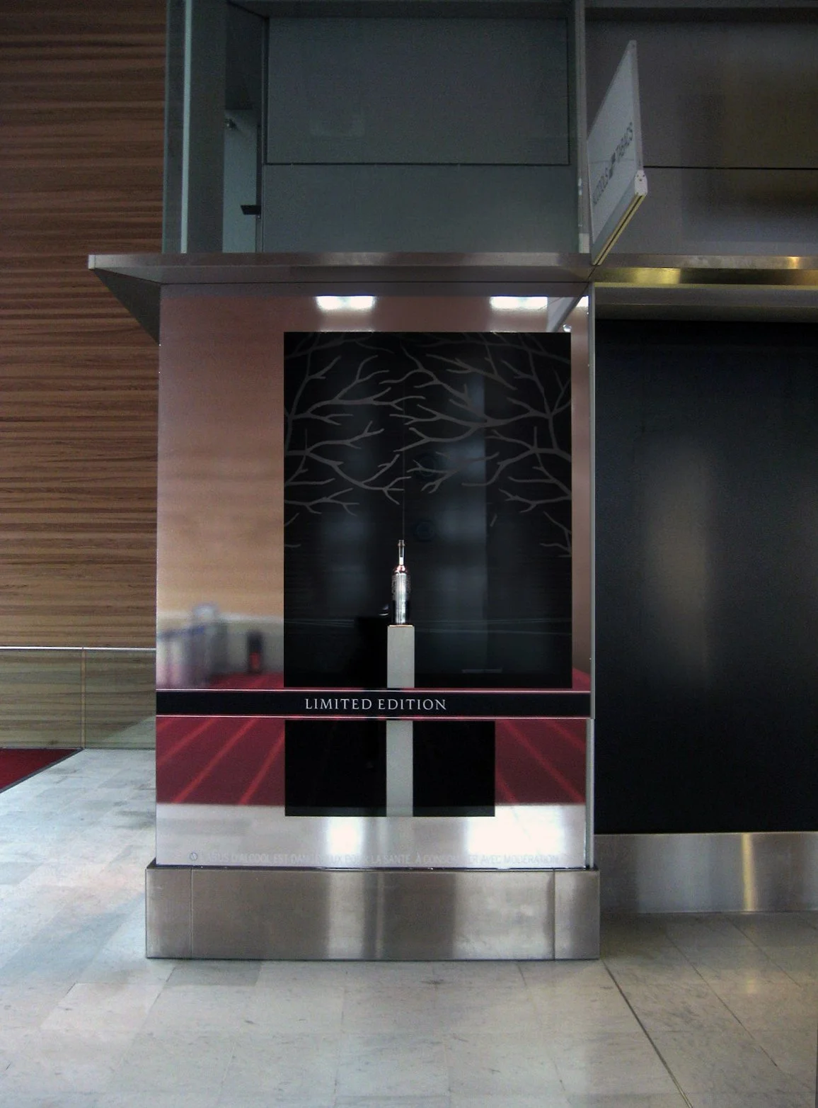 Single Belvedere bottle on a pedestal inside a mirrored airport display with dark tree graphics.