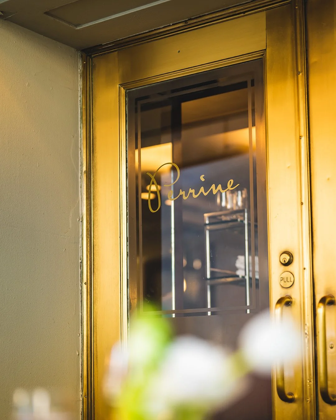 Gold Perrine signature logo on a brass-framed glass restaurant door.