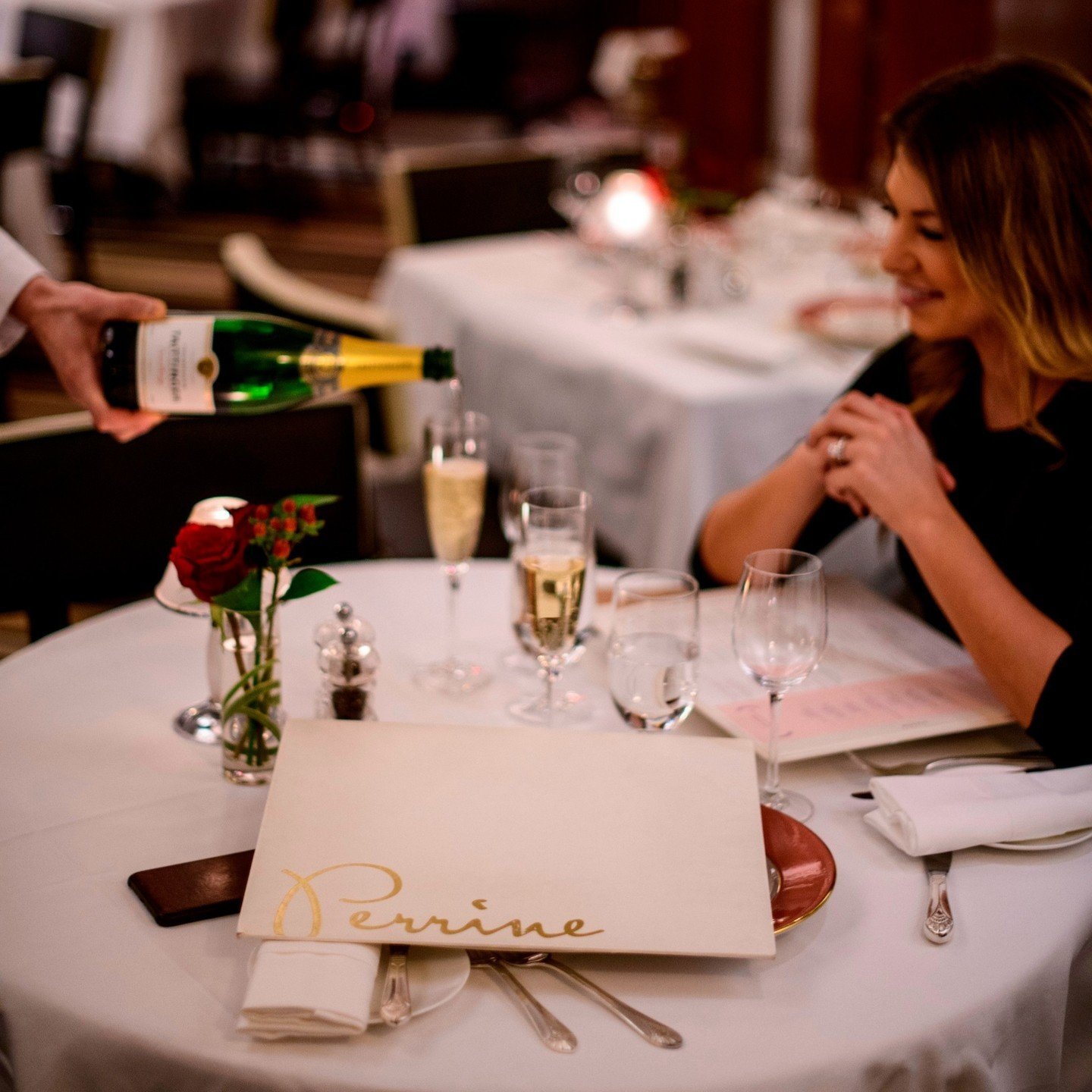 Champagne service at Perrine with a branded menu on the white-clothed dining table.