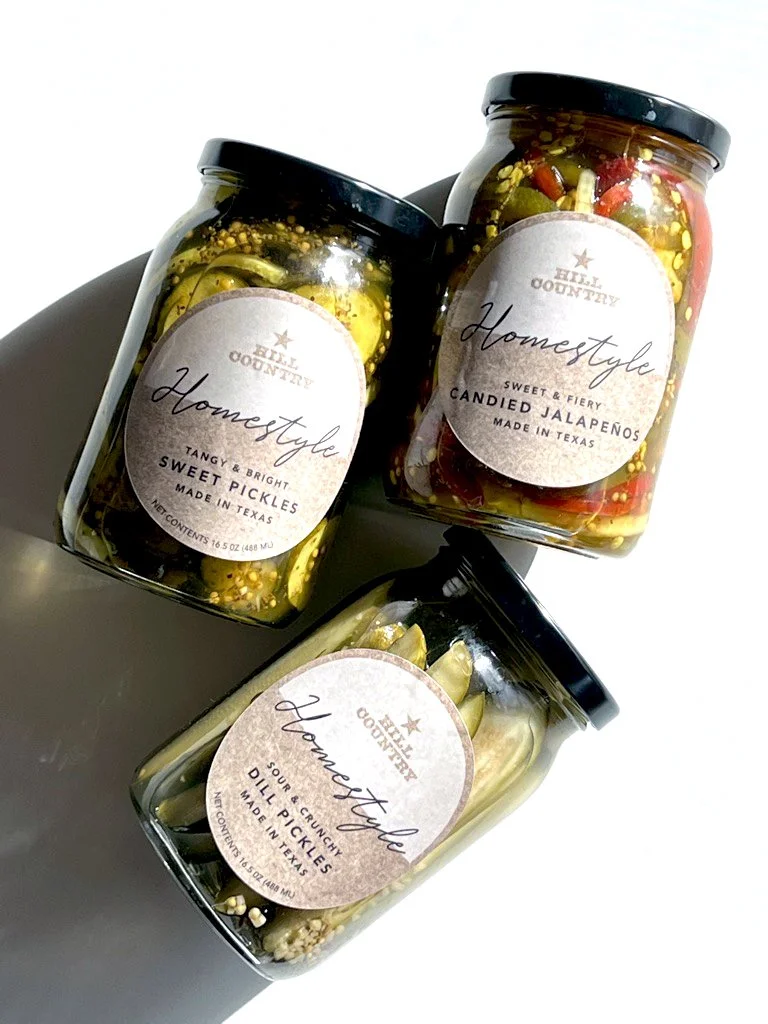 Three Hill Country Homestyle jars of pickles and candied jalapeños photographed together.