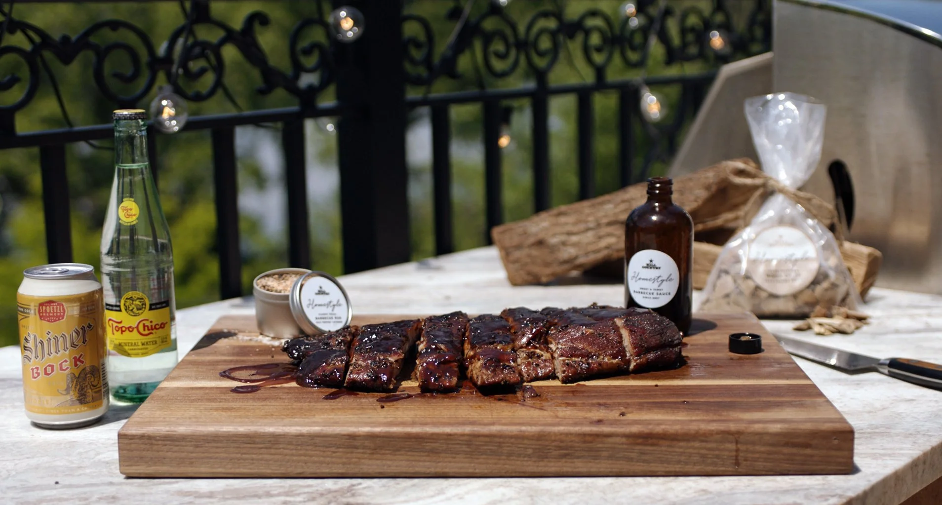 Cooked Hill Country ribs on an outdoor cutting board beside the kit’s sauce, seasoning and smoking-chip bag.