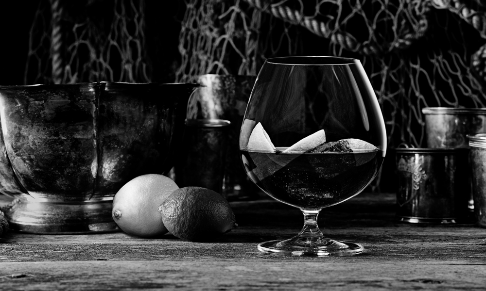 Black-and-white Captain Morgan Black cocktail photograph with a snifter, citrus and metal drinking vessels.