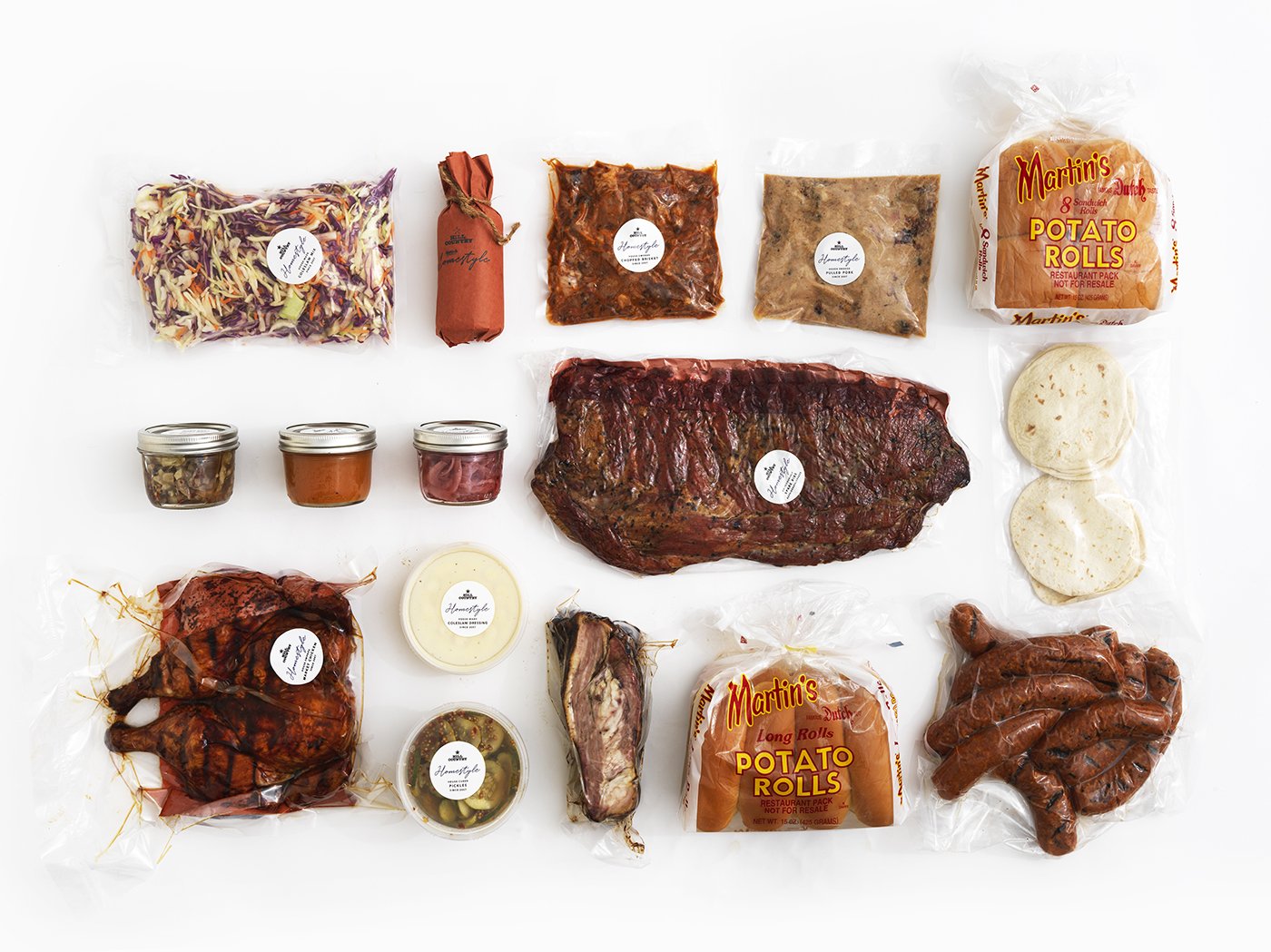 Full Hill Country Homestyle barbecue-box assortment laid out with ribs, meats, rolls, sides, sauces and pickles.