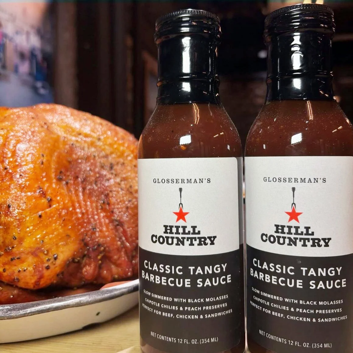Two Hill Country Classic Tangy Barbecue Sauce bottles displayed beside prepared barbecue.