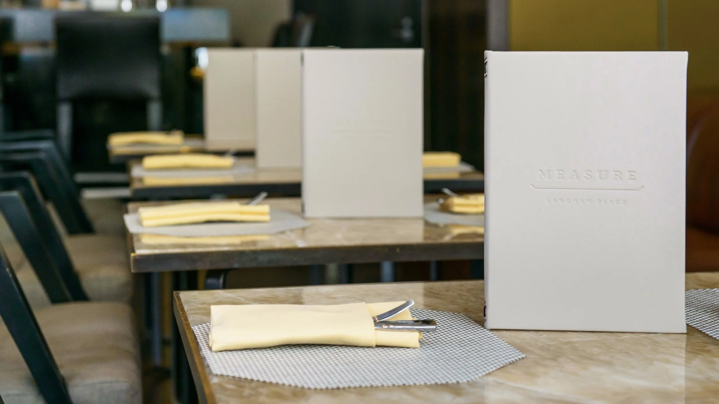 Cream embossed Measure menus standing on set tables inside the lounge.