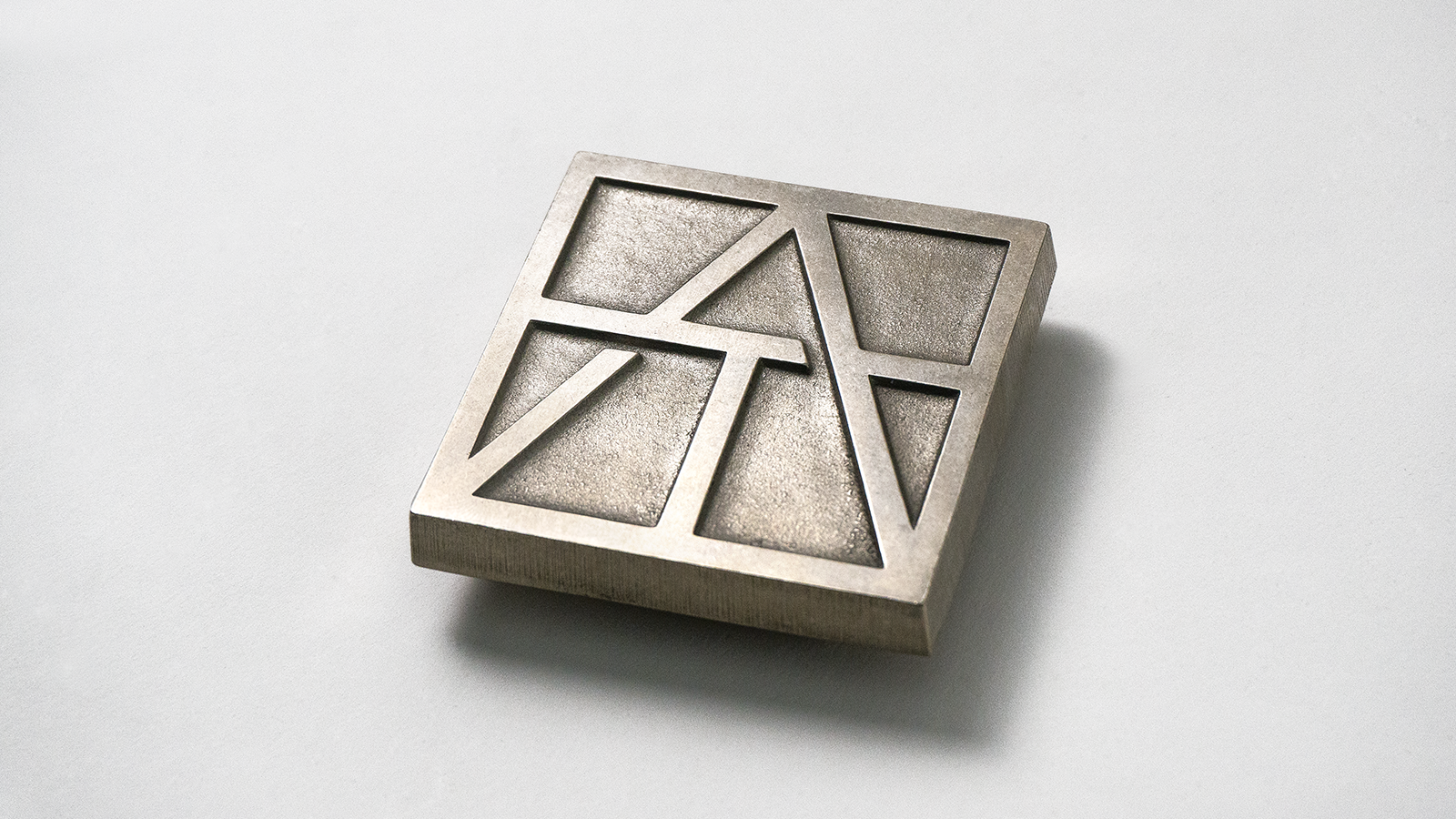 Artistic Tile geometric monogram rendered as a raised metallic tile.