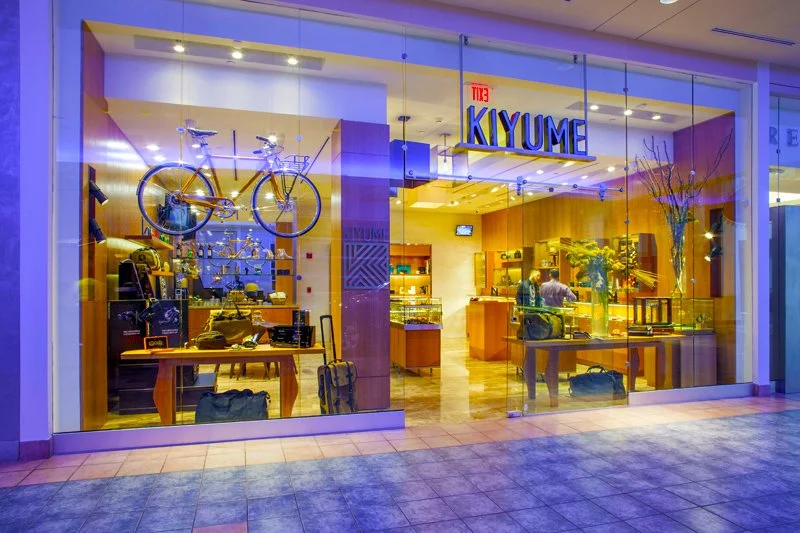 Kiyume storefront with a navy wordmark, glass entrance and a bicycle displayed above the merchandise.